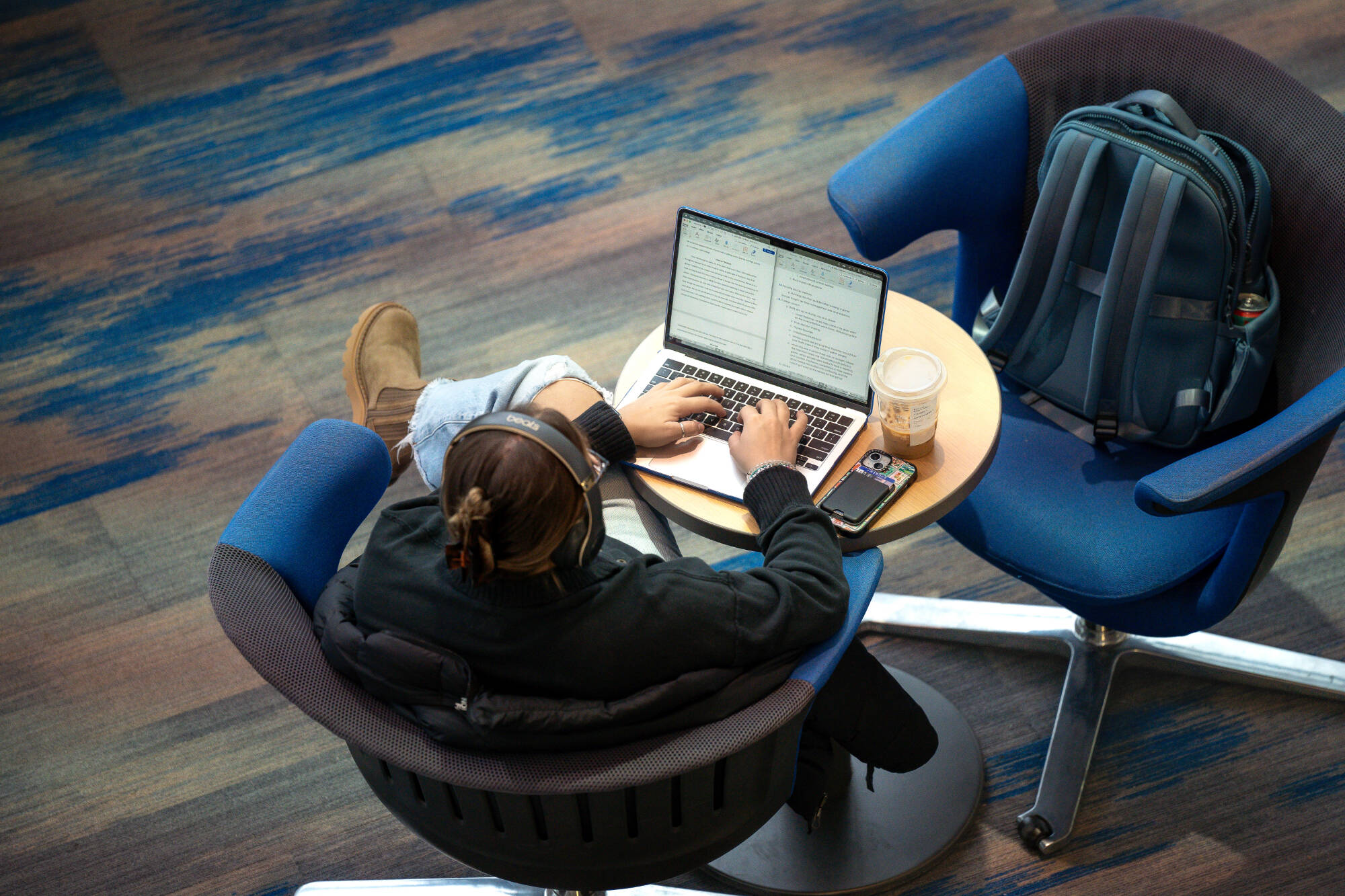 shot of student from above, student is sitting in chair, working on computer, wearing headphones